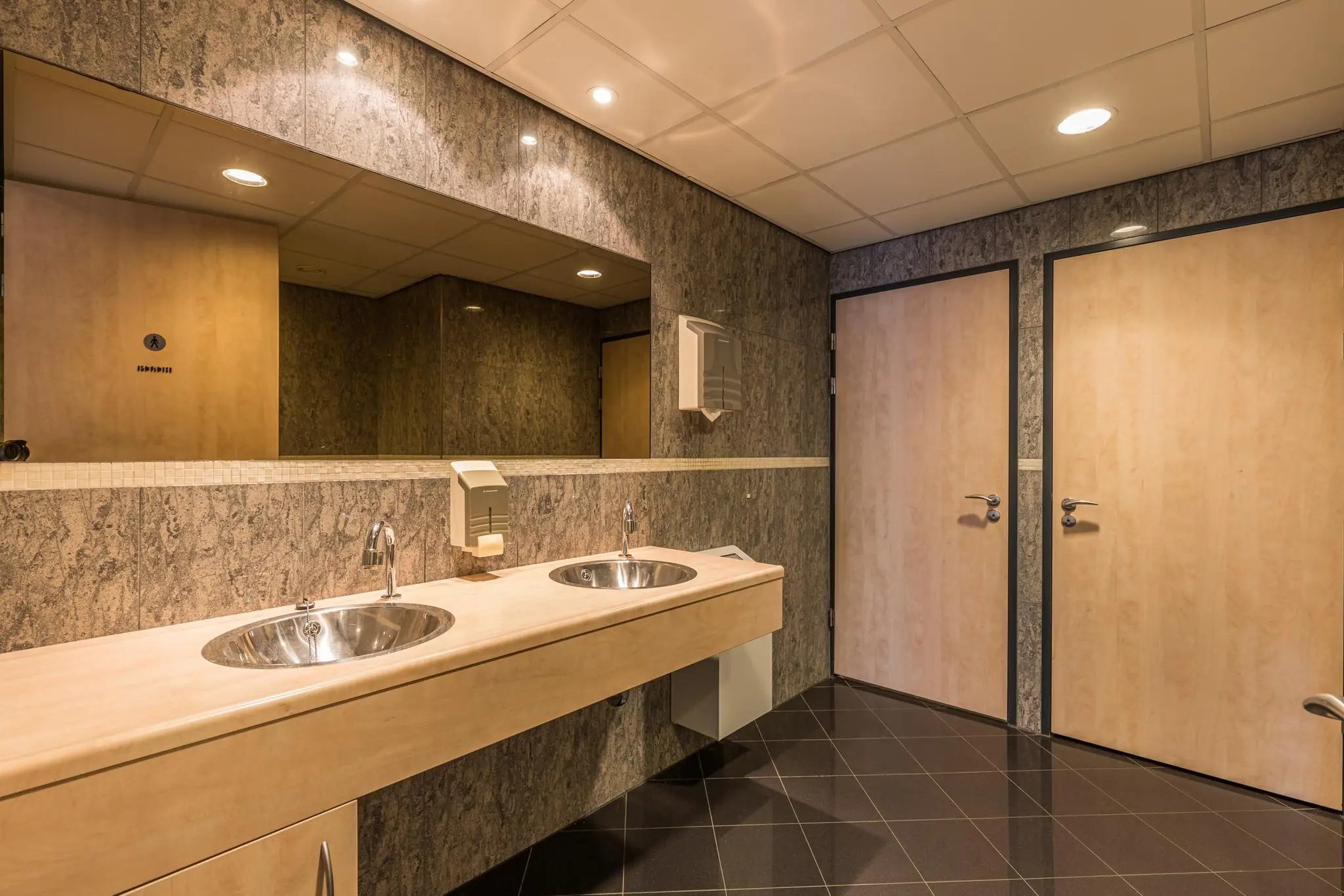 Moderne openbare toiletruimte met twee wasbakken, een grote spiegel en houten deuren aan de Laan Blusse van Oud-Alblas.